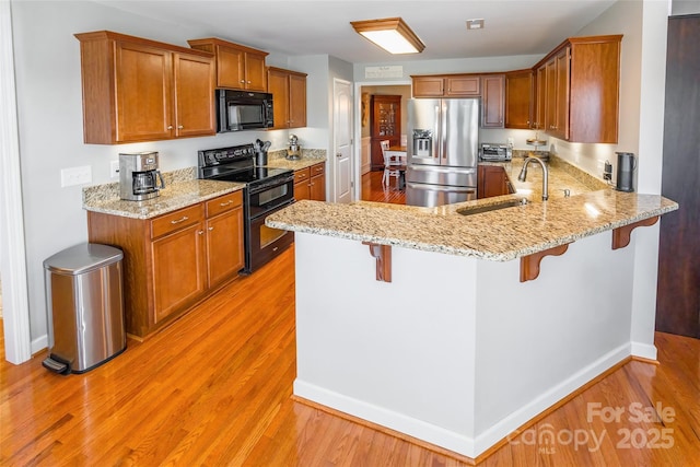 kitchen featuring sink, light stone counters, kitchen peninsula, a breakfast bar area, and black appliances