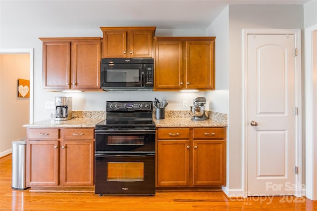 kitchen with light stone counters, black appliances, and light wood-type flooring