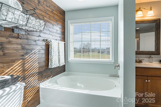 bathroom featuring a bathing tub, vanity, wood walls, and a wealth of natural light