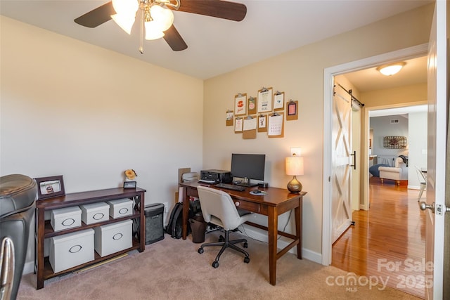 office area with a barn door, ceiling fan, and light carpet