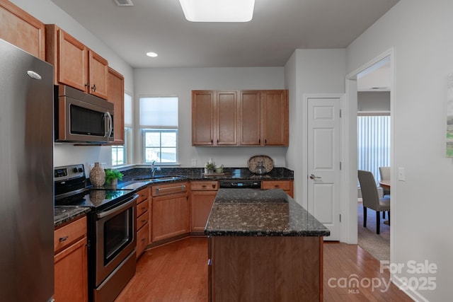 kitchen with sink, dark stone countertops, light wood-type flooring, appliances with stainless steel finishes, and a kitchen island