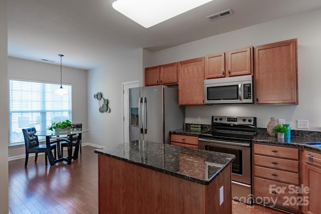 kitchen featuring a kitchen island, pendant lighting, dark hardwood / wood-style flooring, dark stone counters, and stainless steel appliances