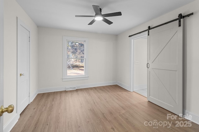 unfurnished bedroom with light wood-type flooring, ceiling fan, and a barn door