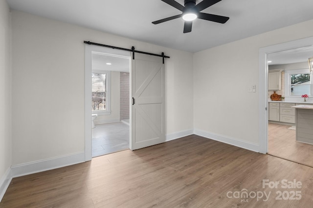 empty room with light hardwood / wood-style floors, ceiling fan, and a barn door