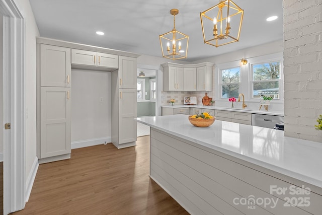 kitchen with pendant lighting, white cabinetry, wood-type flooring, sink, and stainless steel dishwasher