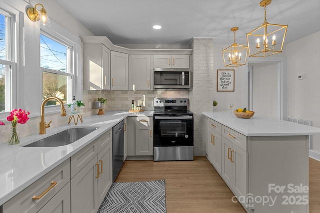 kitchen with appliances with stainless steel finishes, decorative light fixtures, decorative backsplash, sink, and light wood-type flooring