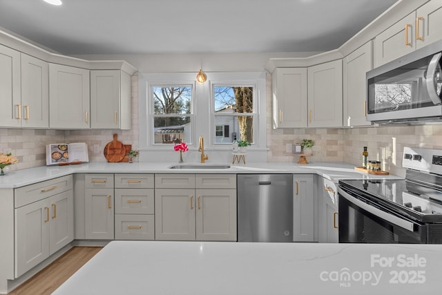 kitchen featuring appliances with stainless steel finishes, decorative backsplash, sink, light hardwood / wood-style floors, and light stone counters