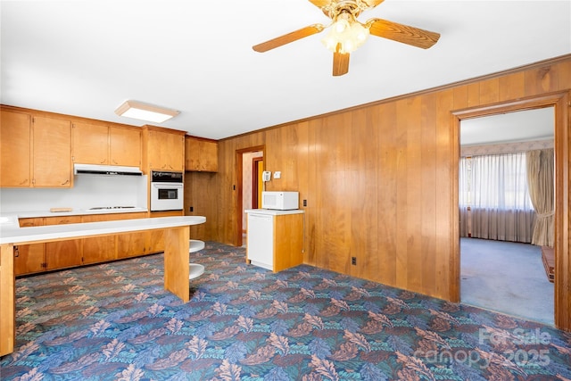 kitchen featuring white appliances, ceiling fan, wooden walls, and dark colored carpet