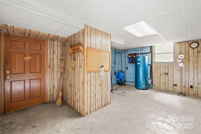 basement featuring a paneled ceiling, water heater, and wooden walls