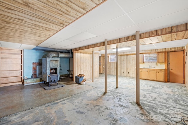 basement with a paneled ceiling, a wood stove, and sink