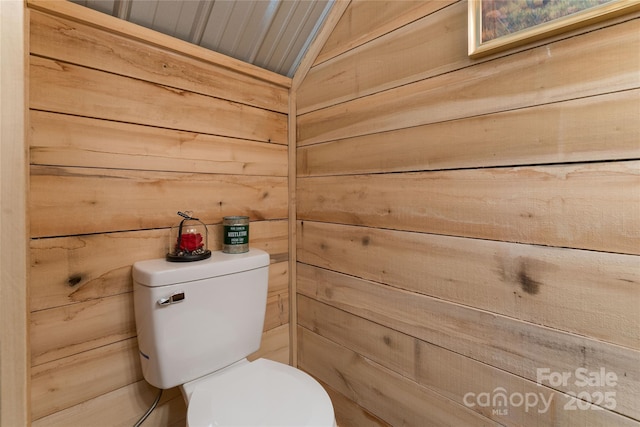 bathroom with vaulted ceiling, wood walls, and toilet