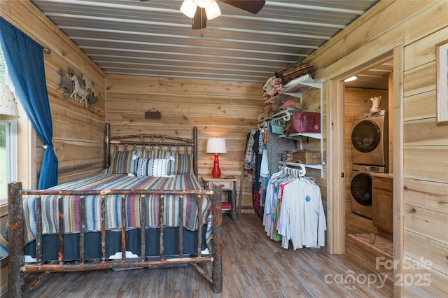 bedroom featuring stacked washer and clothes dryer, ceiling fan, hardwood / wood-style floors, and wood walls