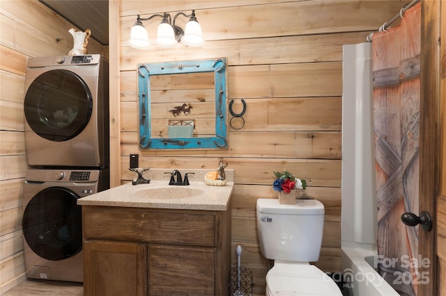 full bathroom featuring wooden walls, stacked washing maching and dryer, shower / tub combo, toilet, and vanity