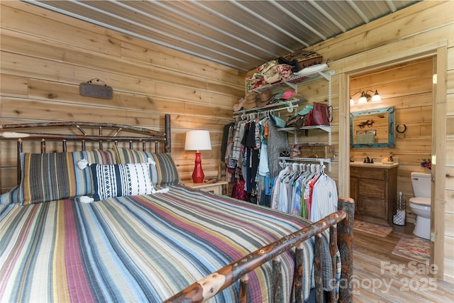 bedroom featuring connected bathroom, a closet, and wood walls