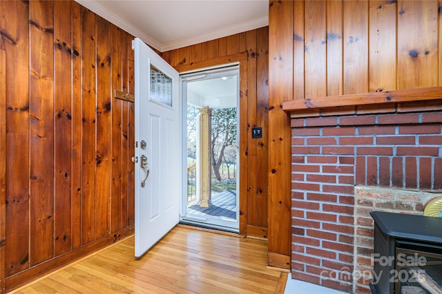 entrance foyer with light wood-type flooring, wooden walls, crown molding, and a wood stove