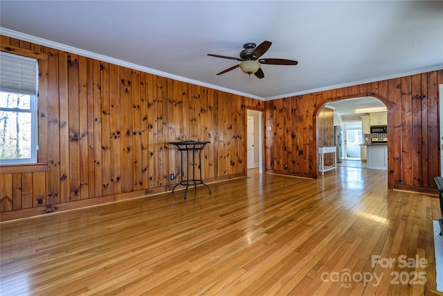 empty room featuring wood walls, ceiling fan, crown molding, and light hardwood / wood-style flooring