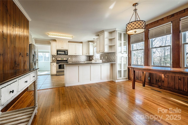 kitchen with appliances with stainless steel finishes, white cabinets, light hardwood / wood-style floors, and decorative light fixtures