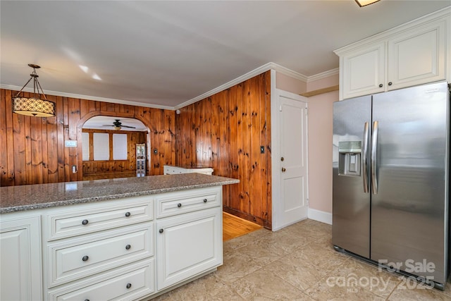 kitchen featuring wooden walls, stainless steel refrigerator with ice dispenser, crown molding, white cabinets, and ceiling fan