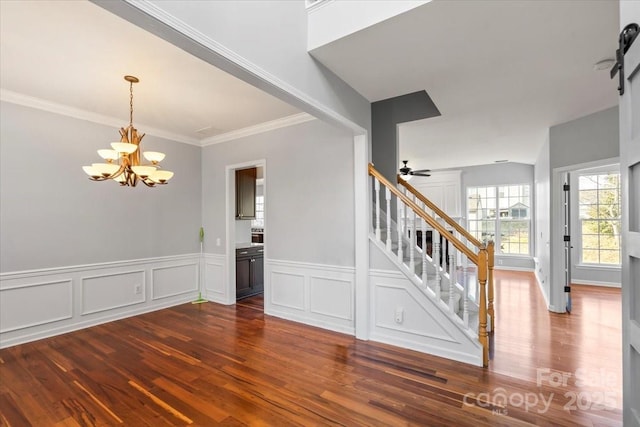 empty room with ornamental molding, ceiling fan with notable chandelier, and dark wood-type flooring