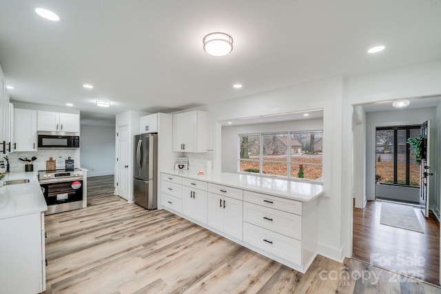 kitchen with decorative backsplash, white cabinetry, light hardwood / wood-style flooring, and appliances with stainless steel finishes