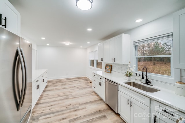 kitchen with backsplash, stainless steel appliances, sink, light hardwood / wood-style floors, and white cabinetry