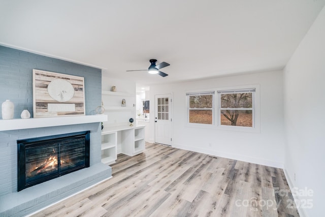 unfurnished living room with built in features, light hardwood / wood-style flooring, a brick fireplace, and ceiling fan