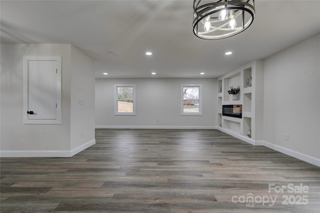 unfurnished living room with dark wood-type flooring, built in features, and a chandelier