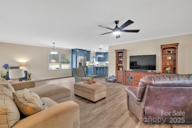 living room with crown molding, a ceiling fan, light wood-type flooring, and baseboards