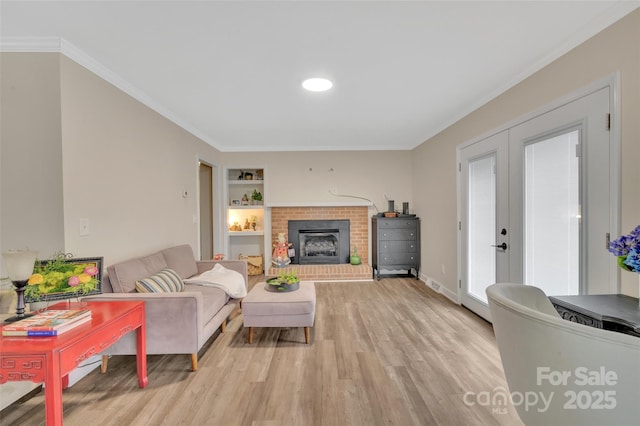 living area featuring a brick fireplace, crown molding, built in features, french doors, and light wood-style floors