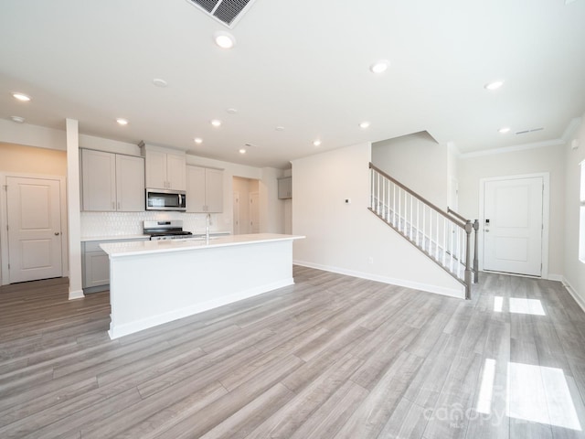 kitchen with backsplash, a kitchen island with sink, light hardwood / wood-style flooring, and appliances with stainless steel finishes