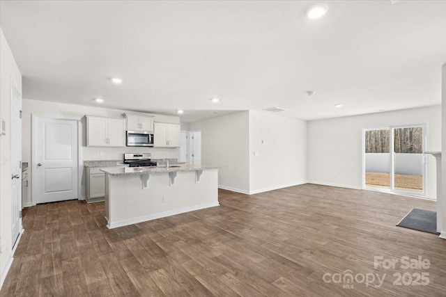 kitchen featuring white cabinets, appliances with stainless steel finishes, a kitchen bar, light stone counters, and a center island with sink