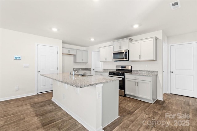 kitchen featuring appliances with stainless steel finishes, a kitchen island with sink, dark hardwood / wood-style flooring, light stone counters, and sink