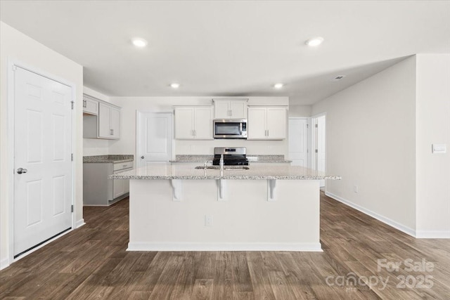 kitchen with a kitchen island with sink, dark wood-type flooring, light stone counters, and stainless steel appliances