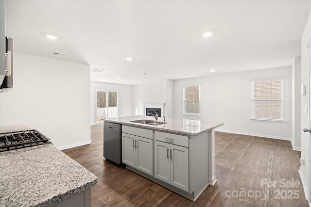 kitchen featuring light stone countertops, an island with sink, sink, gray cabinets, and stainless steel dishwasher