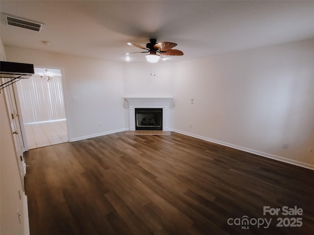 unfurnished living room with ceiling fan with notable chandelier, dark hardwood / wood-style flooring, and a fireplace