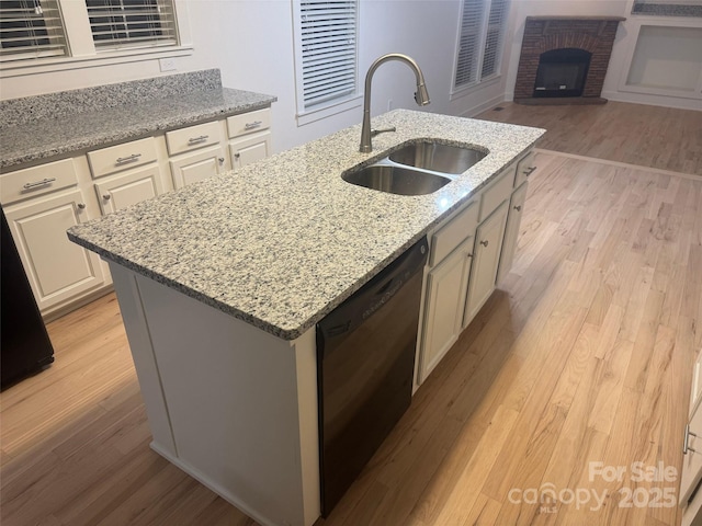 kitchen featuring light stone countertops, sink, a center island with sink, a fireplace, and black dishwasher