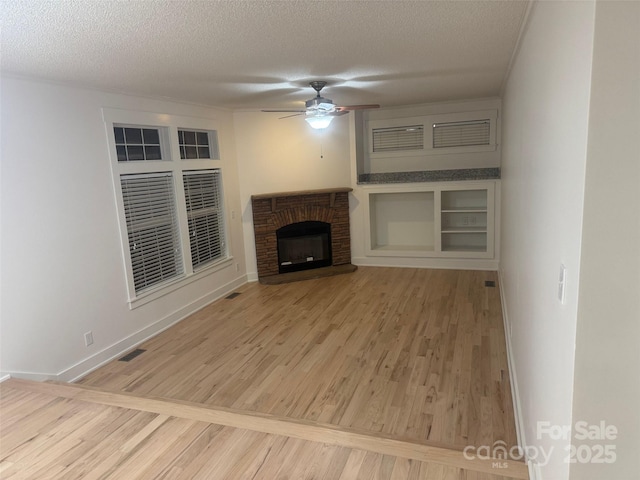 unfurnished living room featuring ceiling fan, a textured ceiling, and a brick fireplace