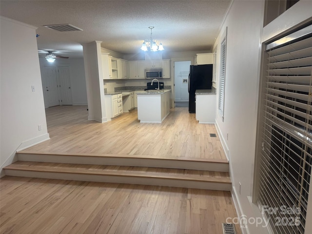 kitchen featuring a center island, white cabinets, black fridge, a textured ceiling, and decorative light fixtures