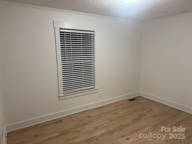 empty room with a textured ceiling, light hardwood / wood-style floors, and crown molding