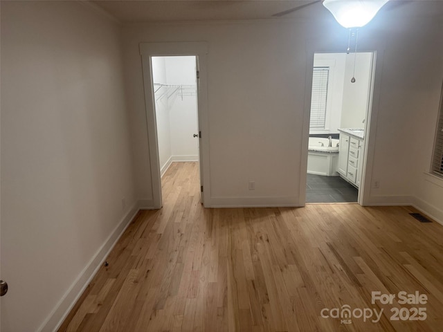 unfurnished bedroom featuring light wood-type flooring, a walk in closet, connected bathroom, and a closet