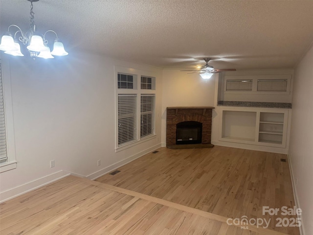 unfurnished living room featuring hardwood / wood-style flooring, ceiling fan with notable chandelier, a textured ceiling, and a brick fireplace