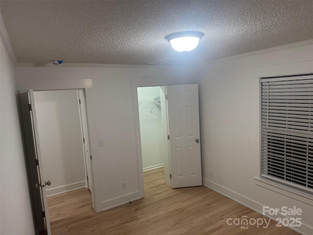 unfurnished bedroom featuring light hardwood / wood-style floors, a walk in closet, crown molding, and a closet