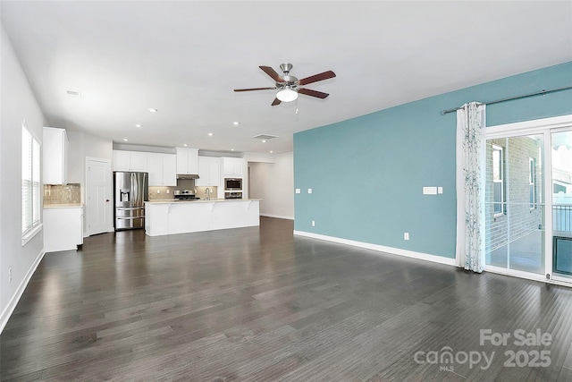 unfurnished living room featuring ceiling fan, a healthy amount of sunlight, dark hardwood / wood-style flooring, and sink