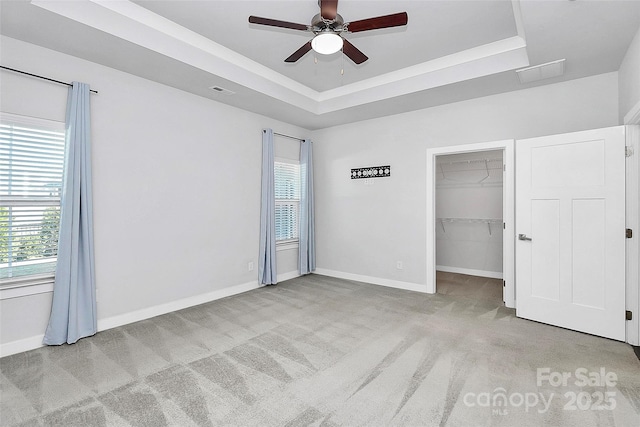 unfurnished bedroom featuring light carpet, a walk in closet, a tray ceiling, ceiling fan, and a closet