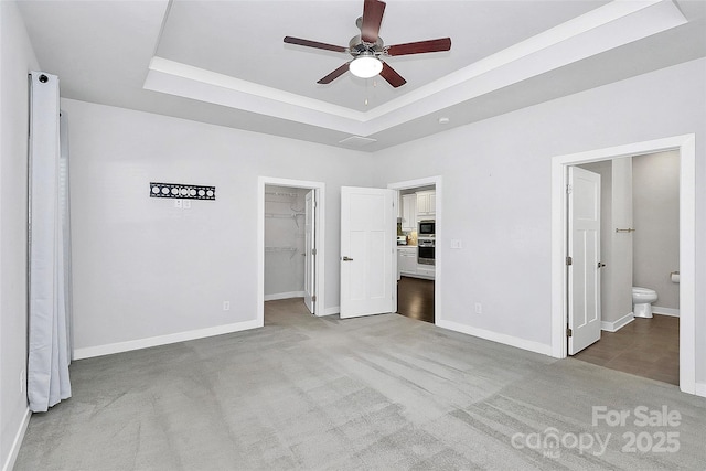 unfurnished bedroom featuring carpet flooring, ensuite bath, ceiling fan, a walk in closet, and a closet