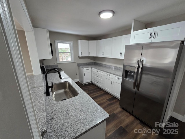 kitchen with light stone counters, sink, stainless steel fridge, and white cabinets