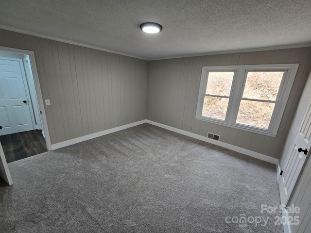 carpeted spare room with ornamental molding, a textured ceiling, and wood walls