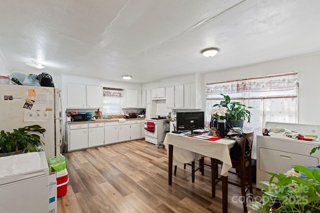 kitchen featuring light wood-type flooring, white cabinetry, a textured ceiling, and white appliances