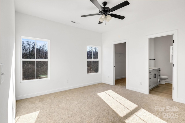 unfurnished bedroom with a walk in closet, light colored carpet, ceiling fan, connected bathroom, and a closet