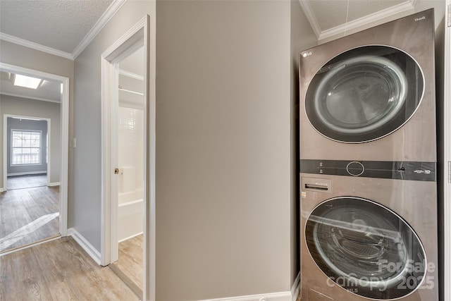 laundry area featuring stacked washer / dryer, light wood-type flooring, a textured ceiling, and ornamental molding